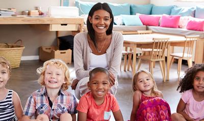 A female teacher poses for a picture with 6 young children.